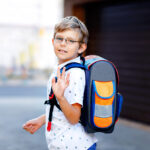 Happy Little Kid Boy With Glasses And Backpack Or Satchel. Schoo